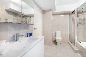 A modern bathroom with a large white sink, a toilet, and a glass-enclosed shower area.