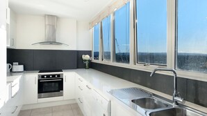 A modern kitchen with white cabinets, a stainless steel oven, a sink, and a large window offering a city view. - Spacious 3 Bedroom Apartment in Surfers Paradise - CoastHM (Surfers Paradise)