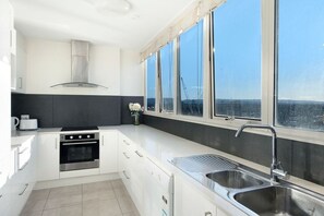 Een moderne keuken met een fornuis, oven en gootsteen, grote ramen met uitzicht, en een vaas met bloemen op het aanrecht.