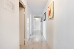A hallway with white walls, a tiled floor, and a door on the left.