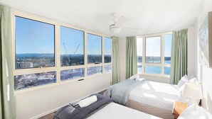 A hotel room with large windows, a bed, a bedside table, and a ceiling fan. - Spacious 3 Bedroom Apartment in Surfers Paradise - CoastHM (Surfers Paradise)