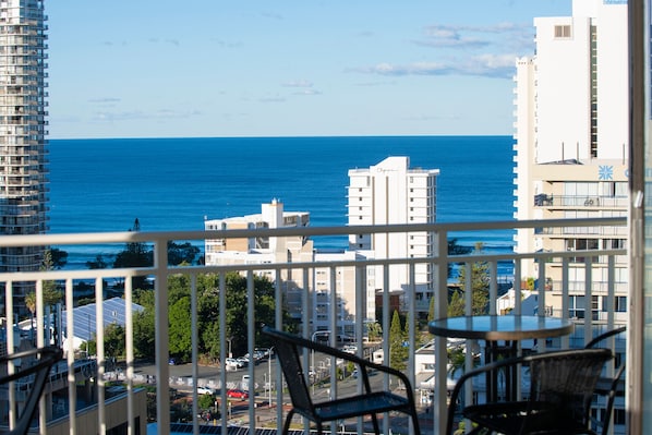 A balcony with a view of the ocean and cityscape, including a tall building and a hotel named 'Olympus'.