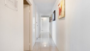 A corridor with white walls, a tiled floor, and a door on the left. - Spacious 3 Bedroom Apartment in Surfers Paradise - CoastHM (Surfers Paradise)