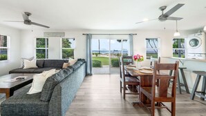 Ein modernes Wohnzimmer mit Sofa, Esstisch und Stühlen, einer Küchenzeile inklusive Waschmaschine sowie großen Fenstern mit Blick ins Freie.