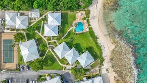Luftaufnahme eines Resorts mit mehreren Gebäuden, einem Swimmingpool und einem Strand.