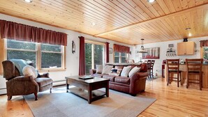 Un salon chaleureux avec un plafond en bois, un canapé, une table basse et un coin repas comprenant des chaises et une table.