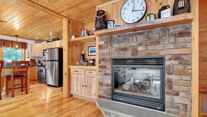 Un intérieur en bois agrémenté d’une cheminée en pierre, d’une horloge et d’un coin cuisine équipé d’appareils électroménagers en acier inoxydable.