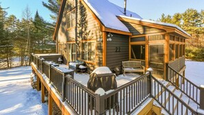 Une cabane en rondins avec une terrasse, un barbecue couvert et une grande fenêtre.