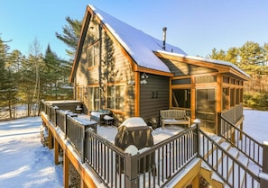 A log cabin with a deck, a covered grill, and a large window.