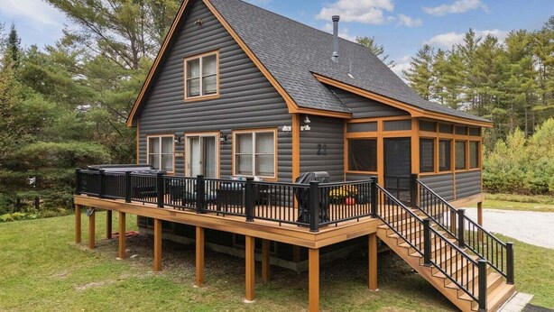 Une cabane en rondins dotée d’une terrasse, d’une cheminée et d’un escalier menant à un deuxième étage.