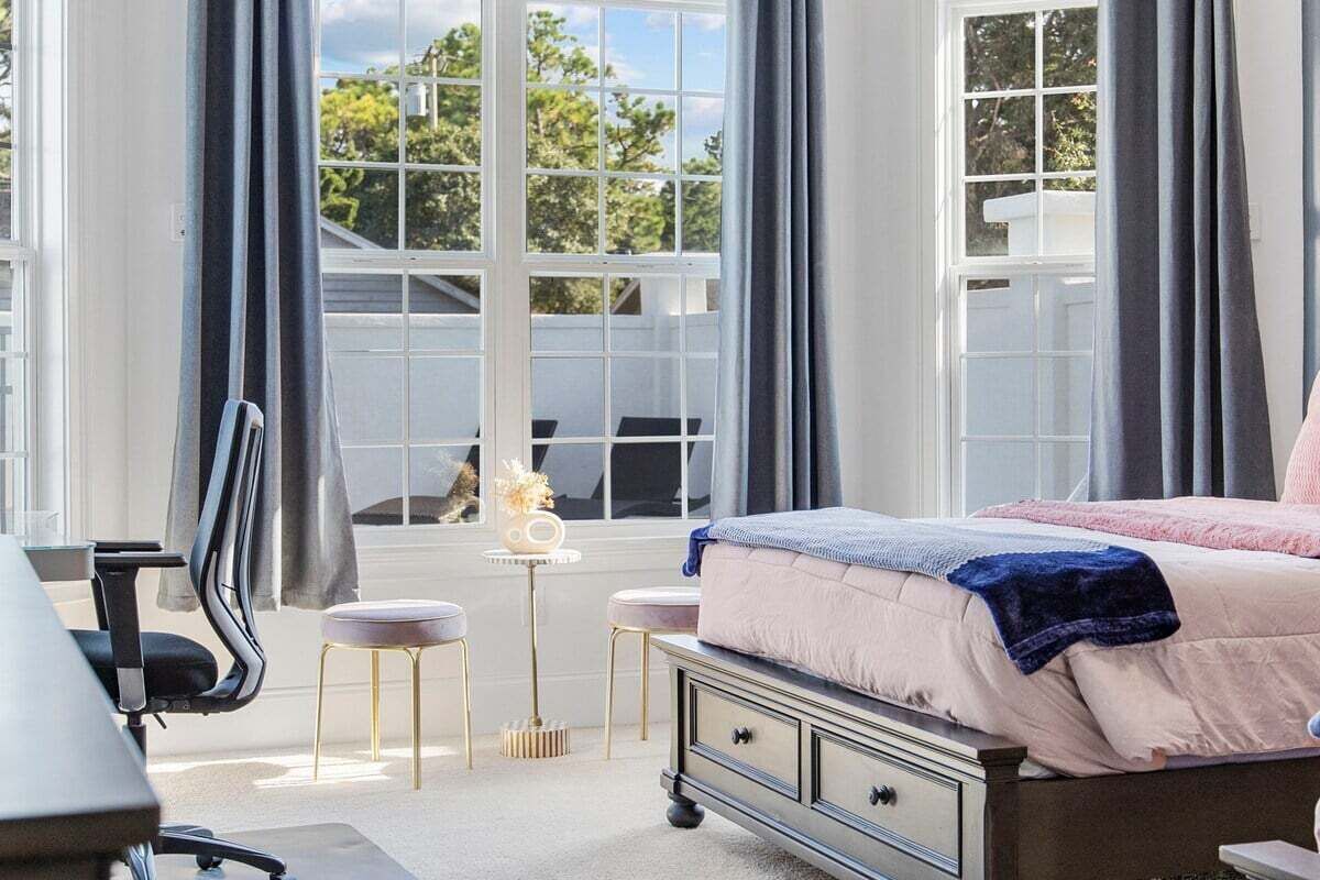 Ein Schlafzimmer mit Bett, Schreibtisch, Stuhl und einem Fenster mit Vorhängen.