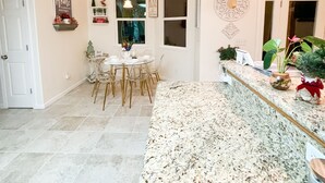 A spacious kitchen with a granite countertop, a dining area with a round table and chairs, and decorative wall art. - Thoughtfully Designed for Accessibility and Family-Friendliness. (Mariposa)