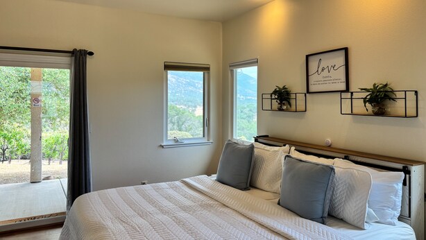 A bedroom with a large bed, two windows, a ceiling fan, and a wall-mounted shelf with plants. - Thoughtfully Designed for Accessibility and Family-Friendliness. (Mariposa)