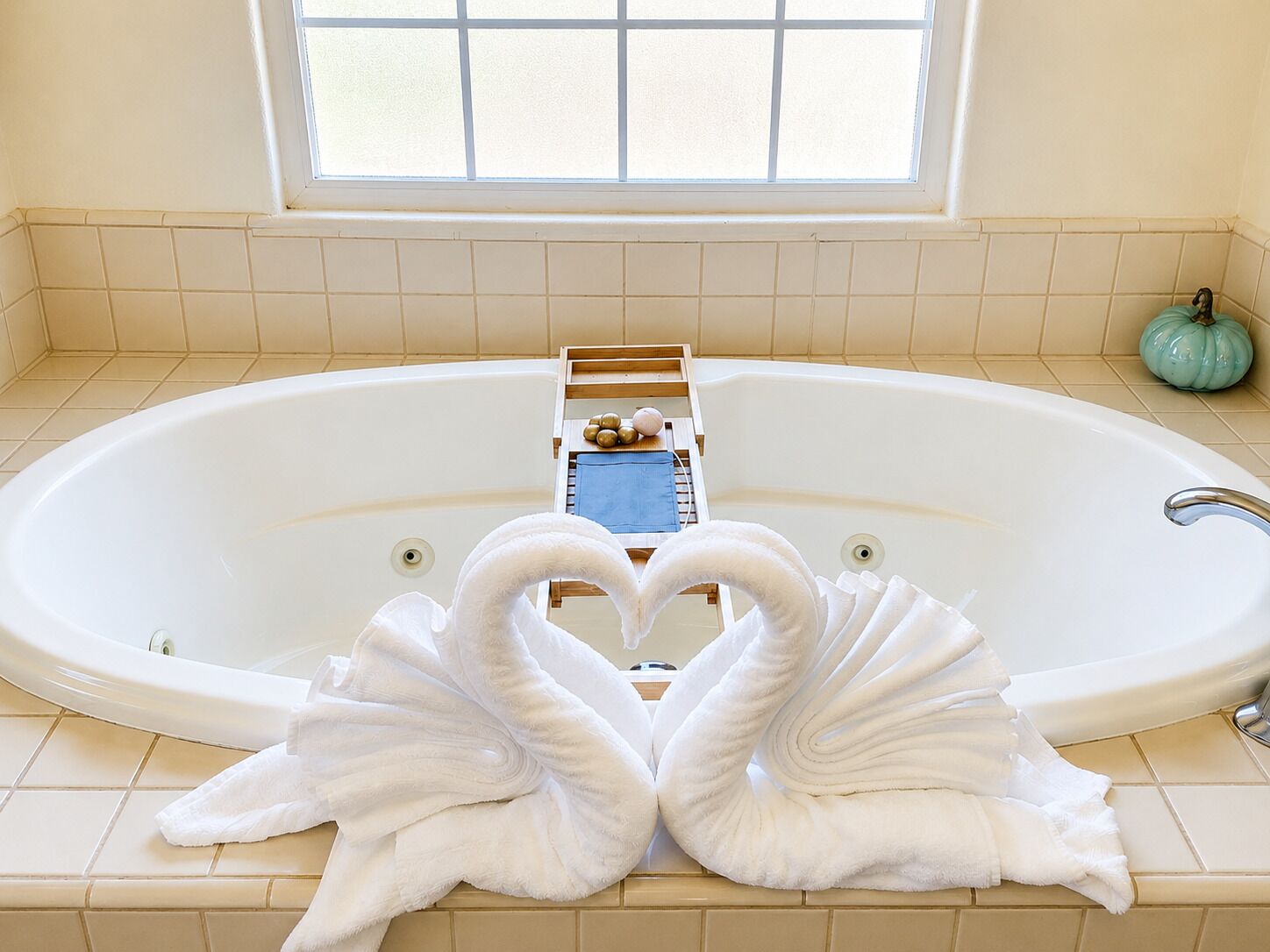 Ein Badezimmer mit einer großen Badewanne, einem Fenster und einer dekorativen Handtuchgestaltung mit dem Motiv eines Schwans.