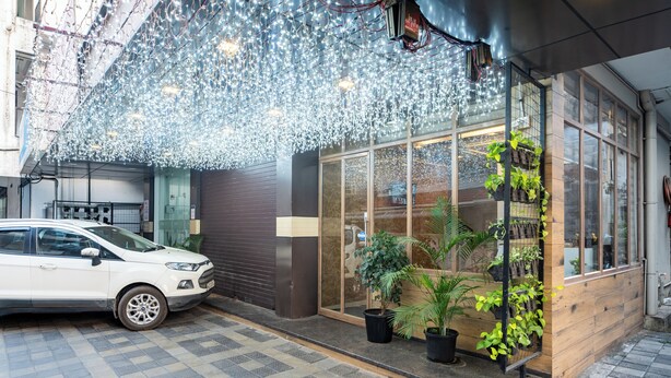 A building entrance with a white car parked outside, a wooden facade, and potted plants near the entrance. - Grace Apart Hotel (Kanayannur)