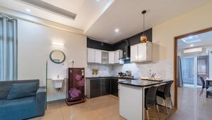 A modern kitchen with a dining area, a sofa, and a small refrigerator. - Grace Apart Hotel (Kanayannur)