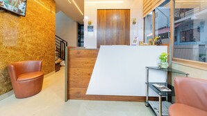 A reception area with a wooden reception desk, a mounted television, and a glass display case with a plant. - Grace Apart Hotel (Kanayannur)