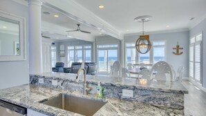 A spacious kitchen with a granite countertop, a stainless steel sink, and a ceiling fan. - Oceanfront 7BR Sleeps 21 Hot Tub, Comm. Pool, 15 steps to the beach, 360 Views! (North Topsail Beach)