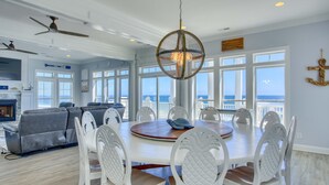A spacious dining area with a round table and white chairs, overlooking a balcony with a view of the ocean. - Oceanfront 7BR Sleeps 21 Hot Tub, Comm. Pool, 15 steps to the beach, 360 Views! (North Topsail Beach)