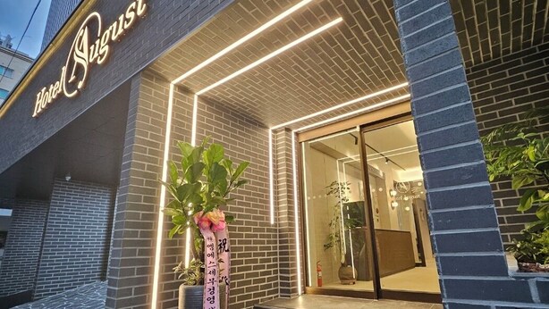 A hotel entrance with a modern brick facade, illuminated signage, and a welcoming entrance with steps and potted plants. - Hwagok August (Seoul)