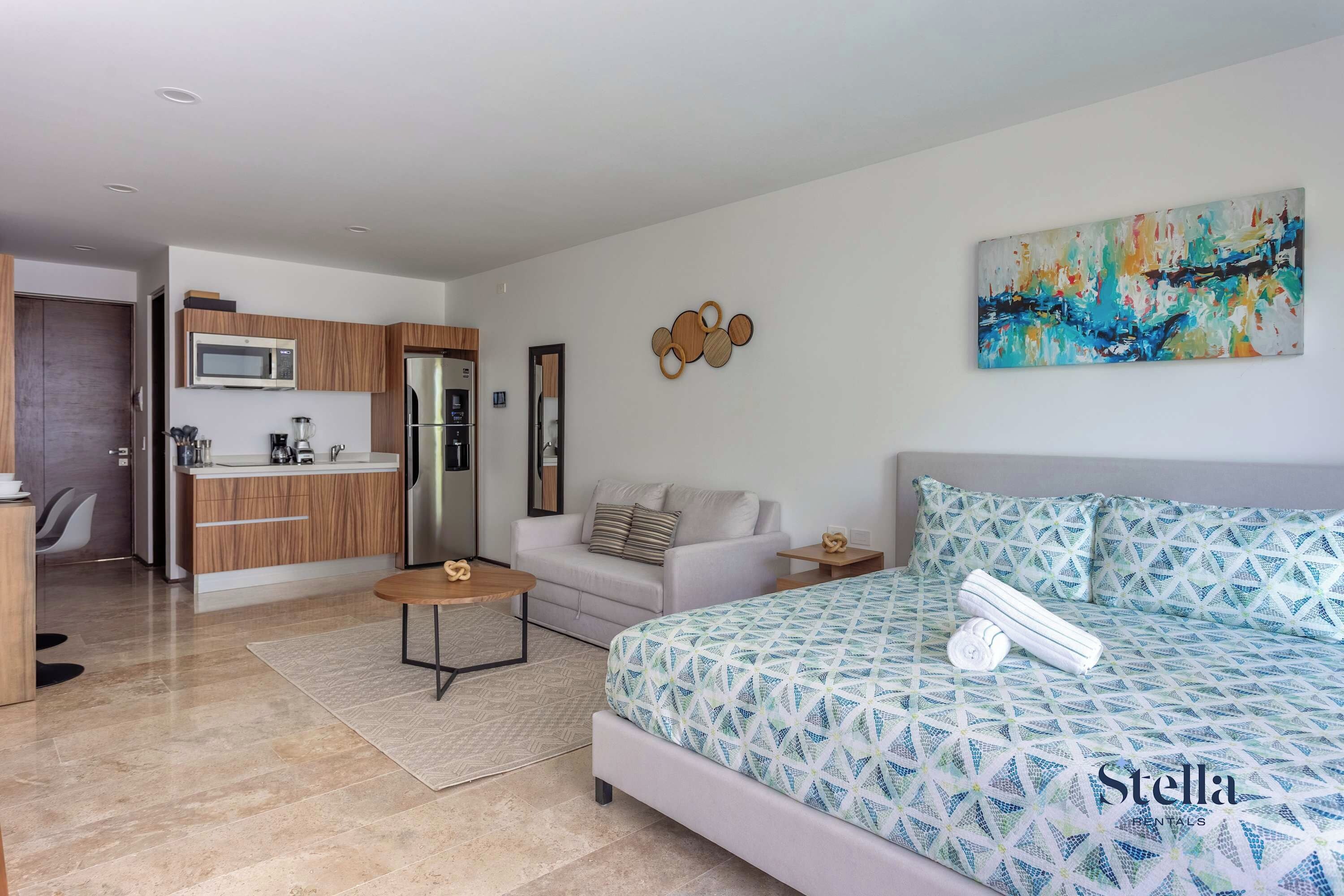 A modern living room with a sofa, a coffee table, and a bed with a geometric patterned duvet.