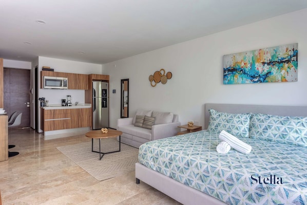 A modern living room with a sofa, a coffee table, and a bed with a geometric patterned duvet.