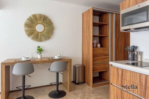 A modern kitchen with a wooden dining table, two bar stools, a decorative wall mirror, and a built-in microwave.