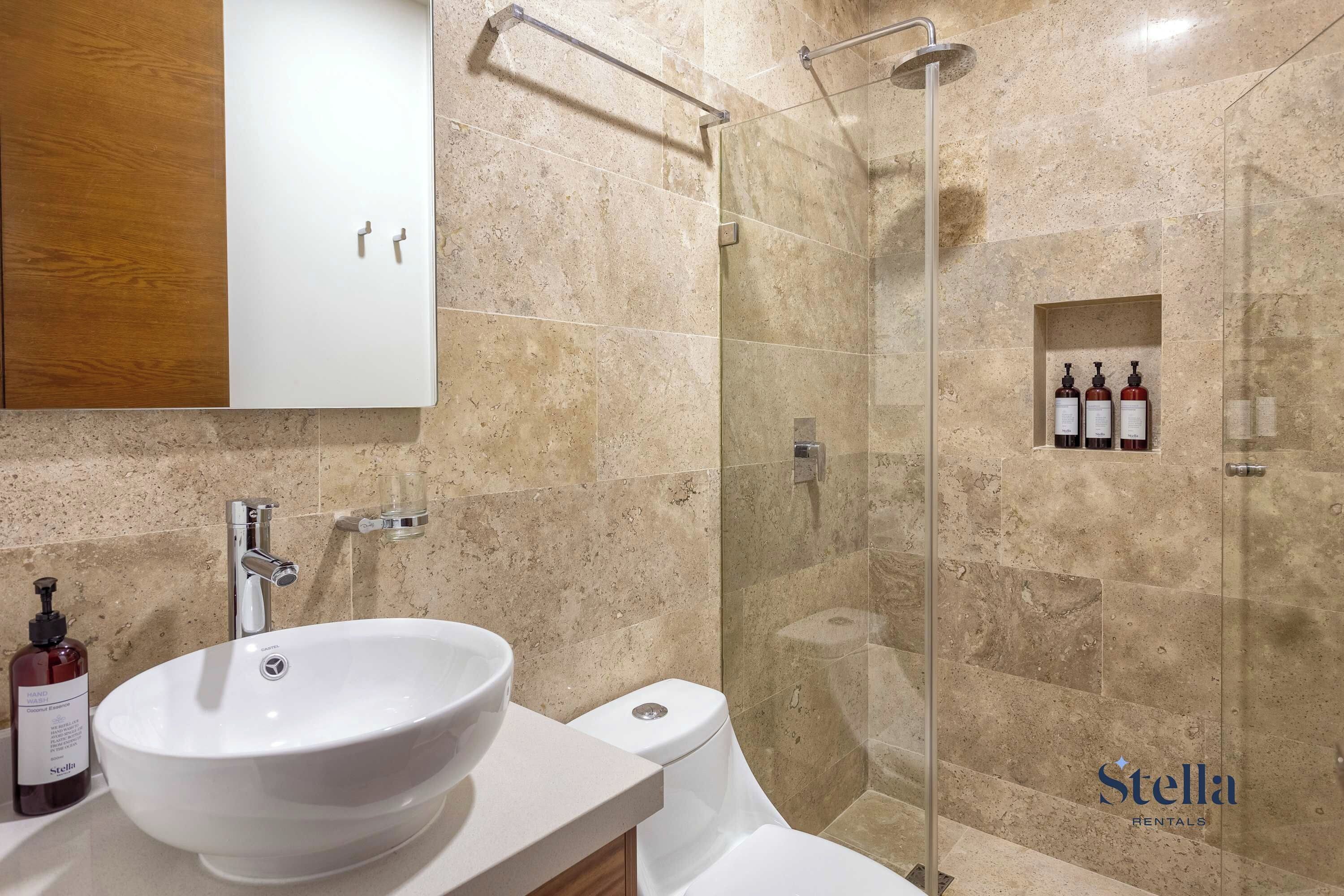 Een badkamer met een wit wastafelmeubel, een spiegel, een douchecabine en een toilet.