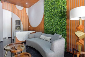 A reception area with a curved grey sofa, wooden tables, a reception desk, and a green vertical garden wall.
