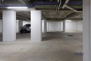 An underground parking garage with white pillars, a single parked car, and fluorescent lighting.