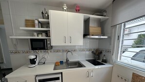 Una cocina compacta con armarios blancos, un microondas, una cafetera Bosch y un lavamanos.