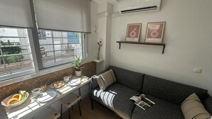 Un espacio habitable compacto con kitchenette, una mesa de comedor con alimentos para el desayuno, un sofá y un estante pequeño con marcos de fotos.