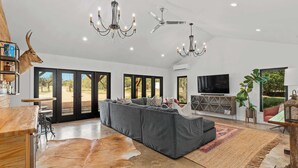 Een ruime woonkamer met een grote grijze modulaire bank, een kroonluchter, plafondventilatoren en een leren vloerkleed.