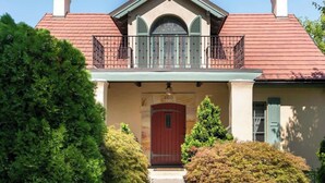 A two-story building with a red door, green shutters, and a balcony with a railing. - High Street Inn W High St Room (Charlottesville)