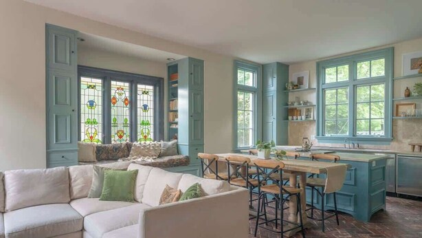 A cozy living room with a white sofa, a dining table with chairs, and a kitchen area with blue cabinets and large windows. - High Street Inn W High St Room (Charlottesville)