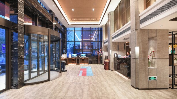A modern hotel lobby with a reception desk, computers, and a large window offering a view of the cityscape.