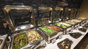 A buffet with various food options in stainless steel containers, arranged on a marble countertop.