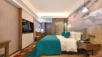 A modern hotel room with a large bed, a desk with a phone, and a painting on the wall.