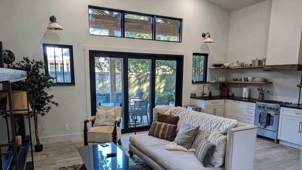 A modern living room with a sofa, coffee table, and a dining area with chairs. There is a kitchen with a stove and cabinets.