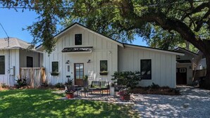 A white single-story building with a front porch, a small garden area, and a gravel driveway.
