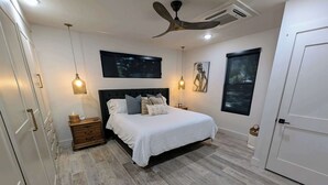 A bedroom with a bed, bedside tables, a ceiling fan, a TV, and a window.