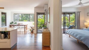 A modern room with a bed, a dining area, and a view of greenery.