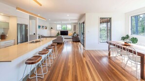 A modern kitchen with a central island, bar stools, a dining area with chairs, and a large window.