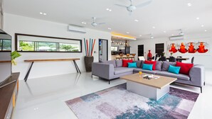 Un salon moderne avec un canapé gris, des coussins colorés, une table basse en bois et une grande fenêtre donnant sur un paysage verdoyant.