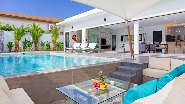 Un espace piscine extérieur moderne, doté de chaises longues, d’une table en verre avec des fruits et d’une terrasse avec un canapé et une table basse.