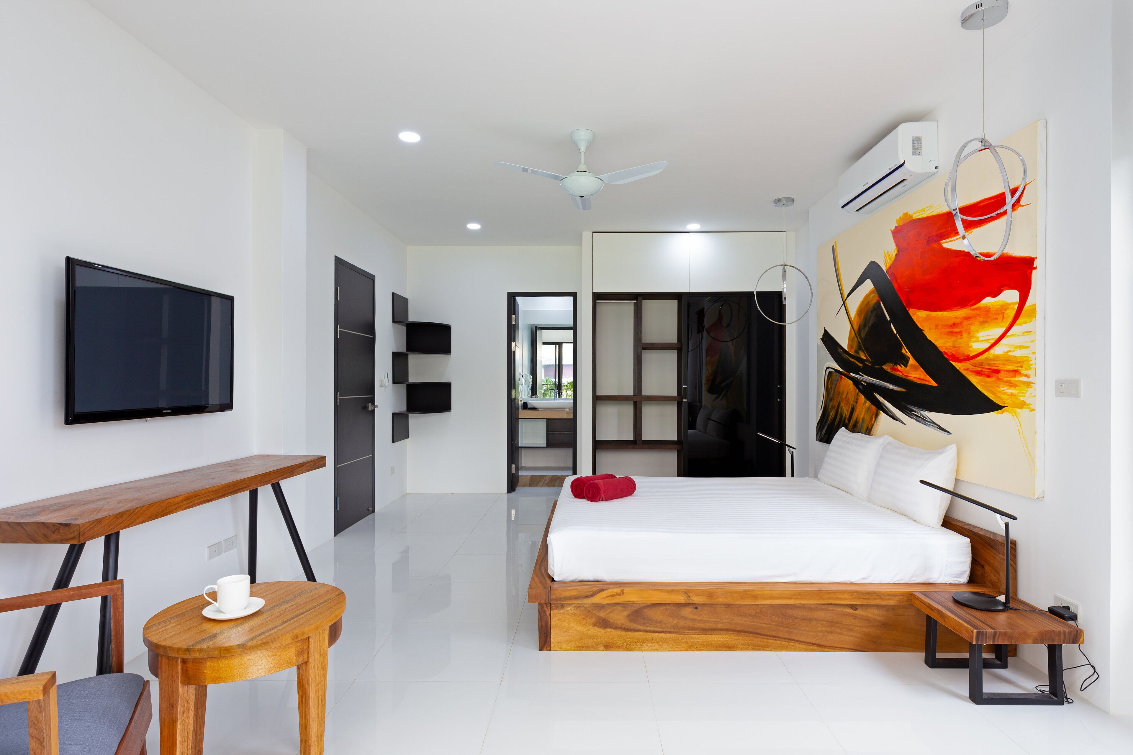 A modern hotel room with a large bed, a desk, a chair, a flat-screen TV, and a painting on the wall.