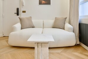 Un salon moderne avec un canapé beige, une petite table blanche et un tableau encadré accroché au mur.