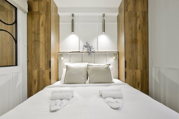 Una cama bien hecha con sábanas blancas, dos almohadas y un par de pantuflas blancas sobre la cama.