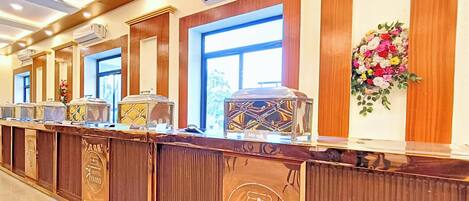 A hotel reception area with a long counter, air conditioning units, and a floral arrangement.