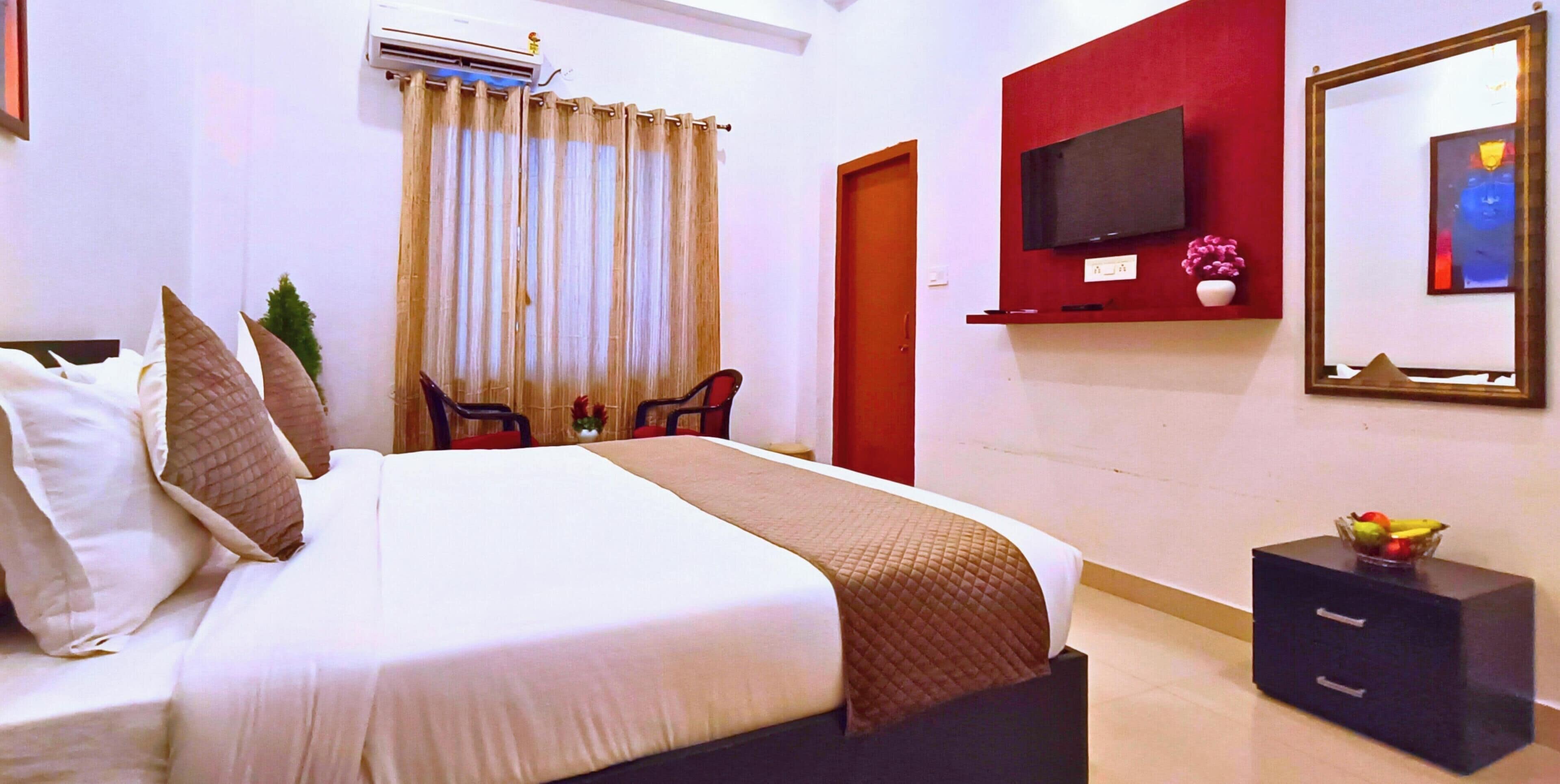 A hotel room with a bed, a television mounted on the wall, a red door, and a small table with a fruit bowl.
